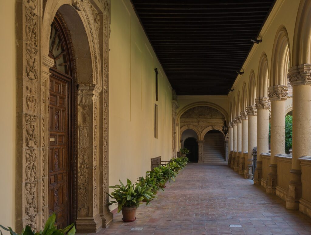 Chiostro di monastero con colonne di pietra e giardino interno illuminato dal sole basso