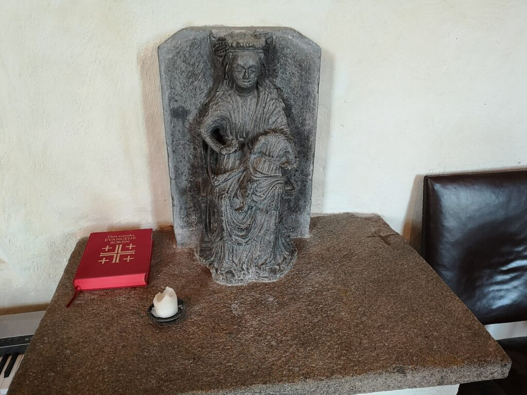Statua lignea della Vergine con il Bambino dal volto scuro, illuminata da candele votive