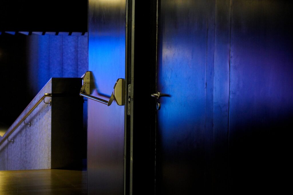 Porta socchiusa su un corridoio illuminato, con una panca di legno addossata al muro