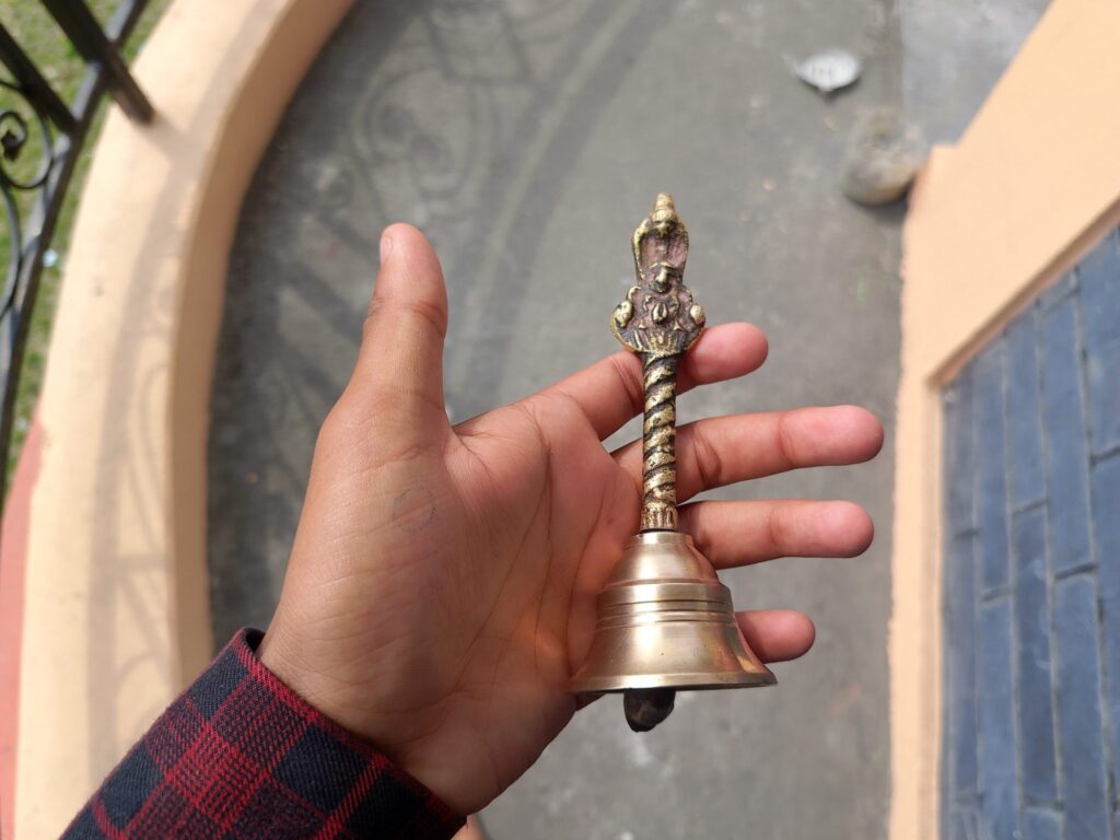 Piccola campana di ottone appoggiata su un ripiano di legno accanto a un battente di feltro