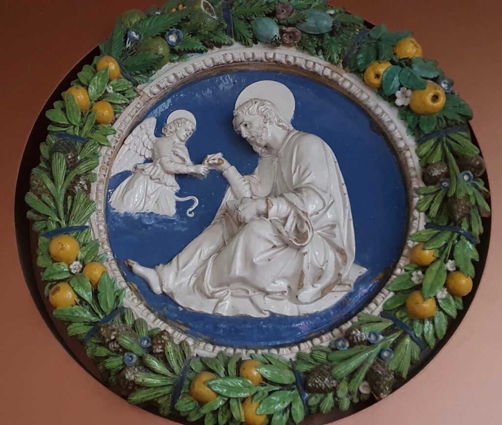 Pala in terracotta invetriata bianca e azzurra con figure a rilievo dentro una cornice di festoni