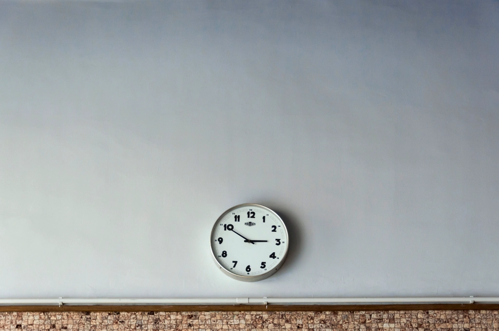 Orologio da parete con lancette nere e quadrante bianco fissato su un muro spoglio