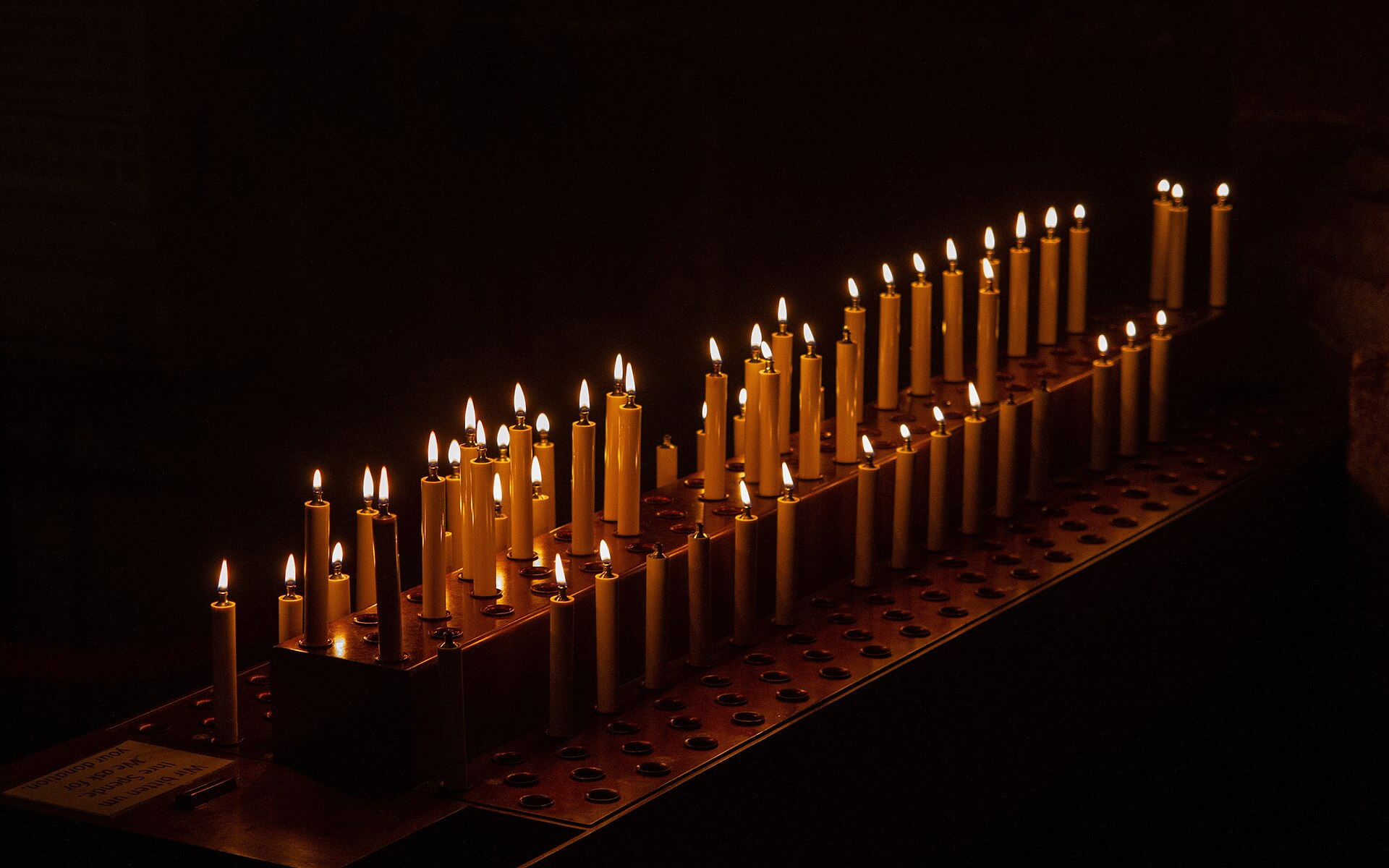 Candele accese davanti a un altare in una cappella in penombra con poche sedie vuote