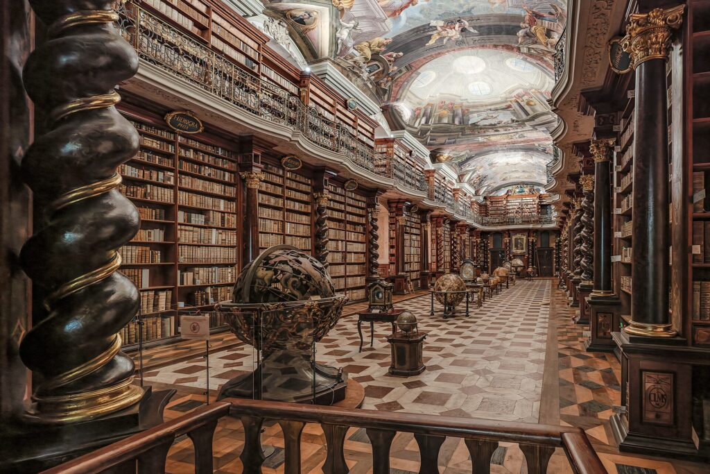 Sala di biblioteca con scaffali di legno su due ordini, ballatoio e soffitto dipinto