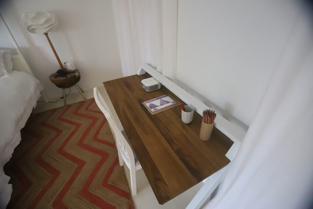 Sedia di legno accostata a un letto, con pochi oggetti appoggiati sul comodino accanto